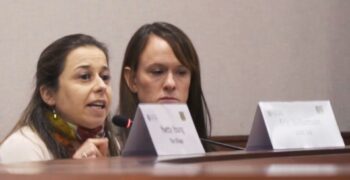 two women sitting at a table with name signs in front of them. one woman speaking.