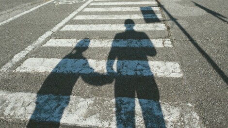 A shadow cast on a crosswalk of a man holding a little girl's hand